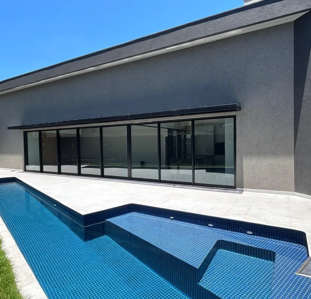 Parede de vidro de uma casa contemporânea com película de controle solar aplicada, vista da área da piscina.