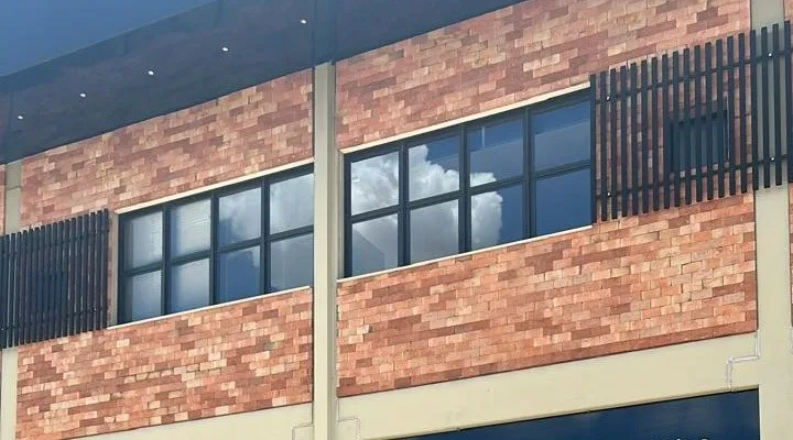 Fachada de prédio comercial em tijolo aparente com janelas em fita cobertas por película escura refletindo as nuvens.