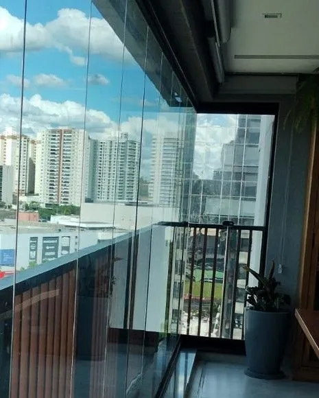Cortina de vidro de sacada de apartamento com película aplicada, com a cidade ao fundo.